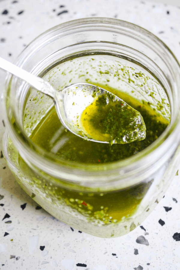 Top down shot of basil oil with spoon in small glass jar. 