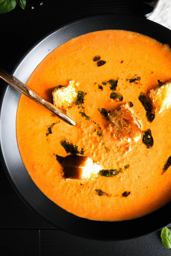 Close-up top down shot of creamy tomato soup topped with grilled cheese croutons and drizzled with basil oil. 