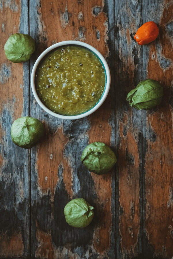 salsa in a small bowl on a distressed wood table surrounded by tomatillos and a habanero pepper