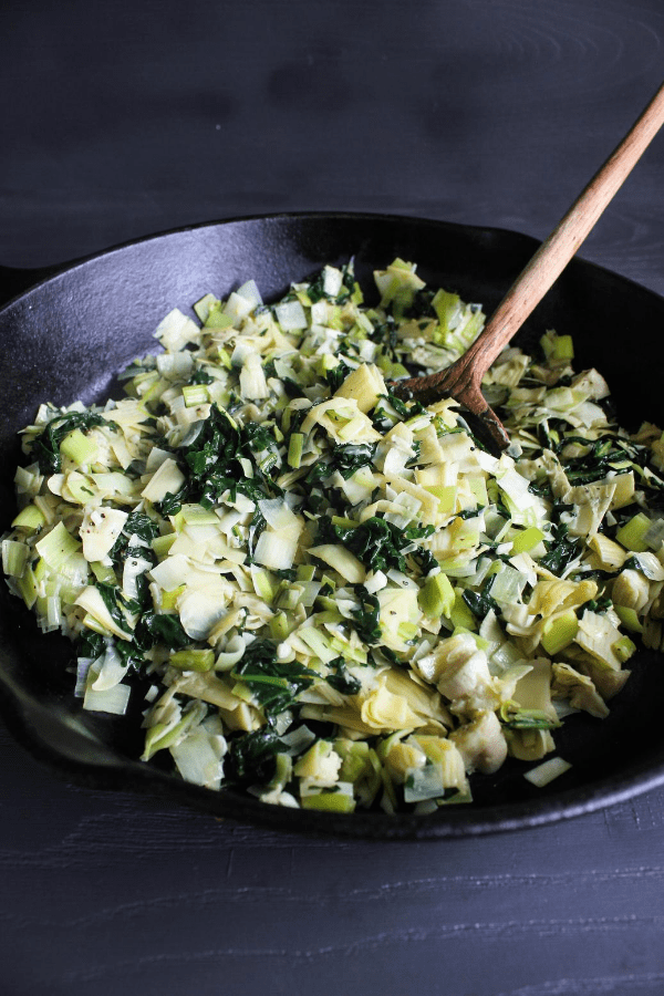 Large cast-iron skillet filled with sautéed spinach, artichokes, and leeks. 