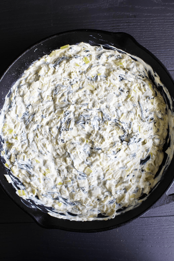 Top down shot of spinach artichoke dip in cast-iron skillet prior to being topped with cheese. 