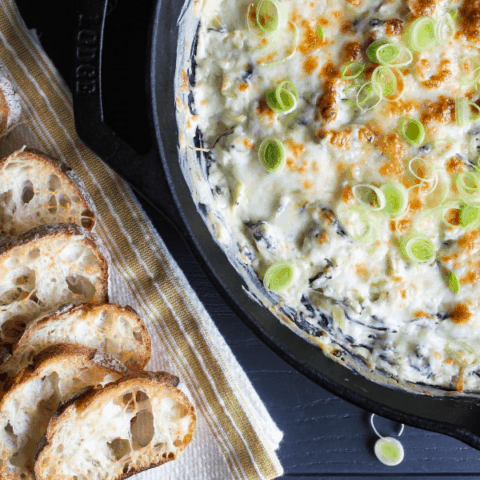 Top down shot of goat cheese spinach artichoke dip in cast-iron skillet with a napkins layered with baguette slices.