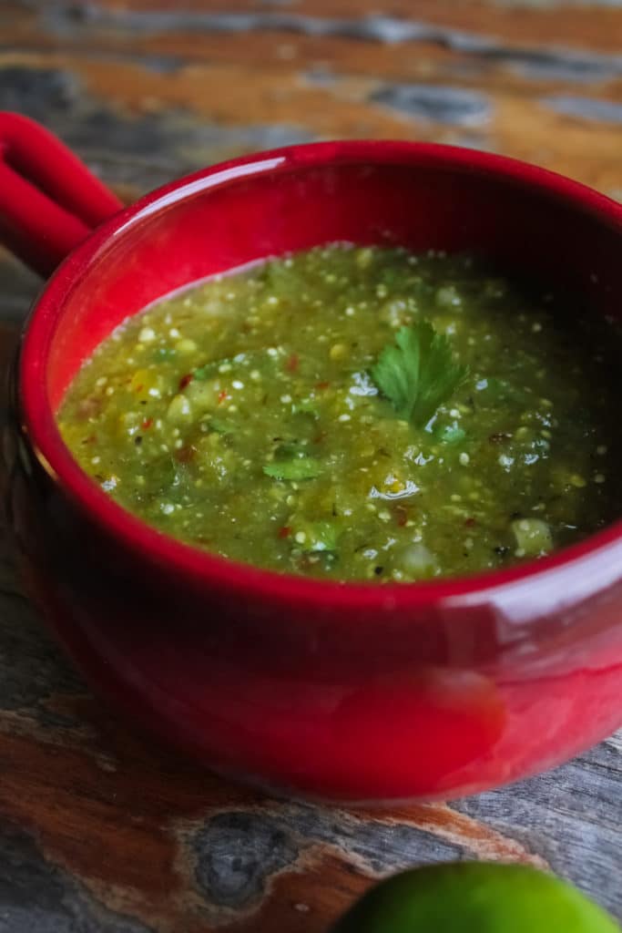 salsa verde in red bowl with lime on table 