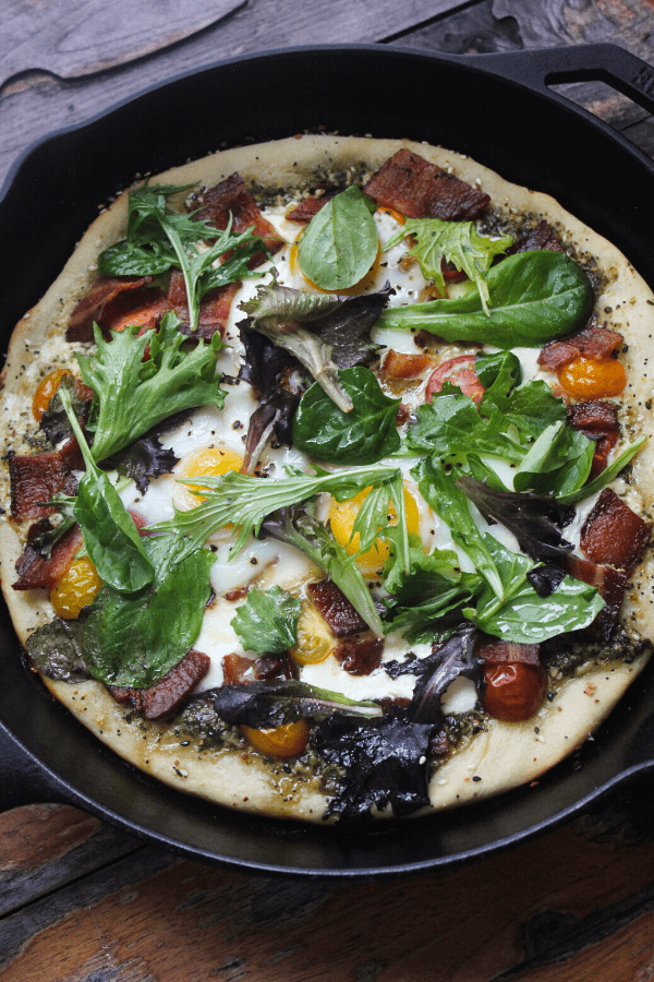 Breakfast BLT pizza cooked in cast-iron skillet made with everything bagel seasoning, pesto, fresh mozzarella, tomatoes, bacon, eggs, and fresh greens.