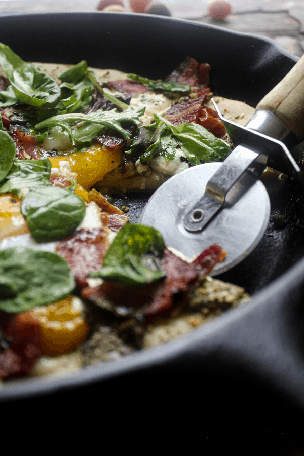 Breakfast BLT pizza cooked in cast-iron skillet made with everything bagel seasoning, pesto, fresh mozzarella, tomatoes, bacon, eggs, and fresh greens.