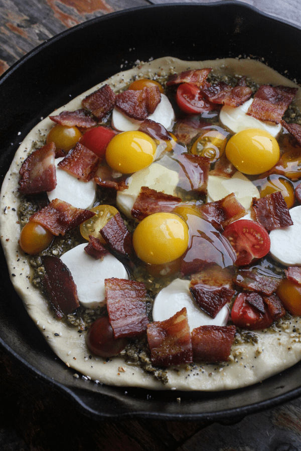 Breakfast BLT cast-iron pizza topped with fresh mozzarella, tomatoes, bacon, and raw eggs. 