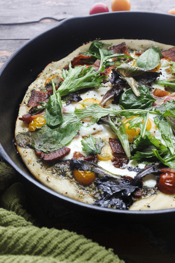 This breakfast BLT cast-iron pizza starts with a homemade dough sprinkled with everything bagel seasoning, is slathered in pesto, and topped with fresh mozzarella, tomatoes, bacon, eggs, and fresh greens.
