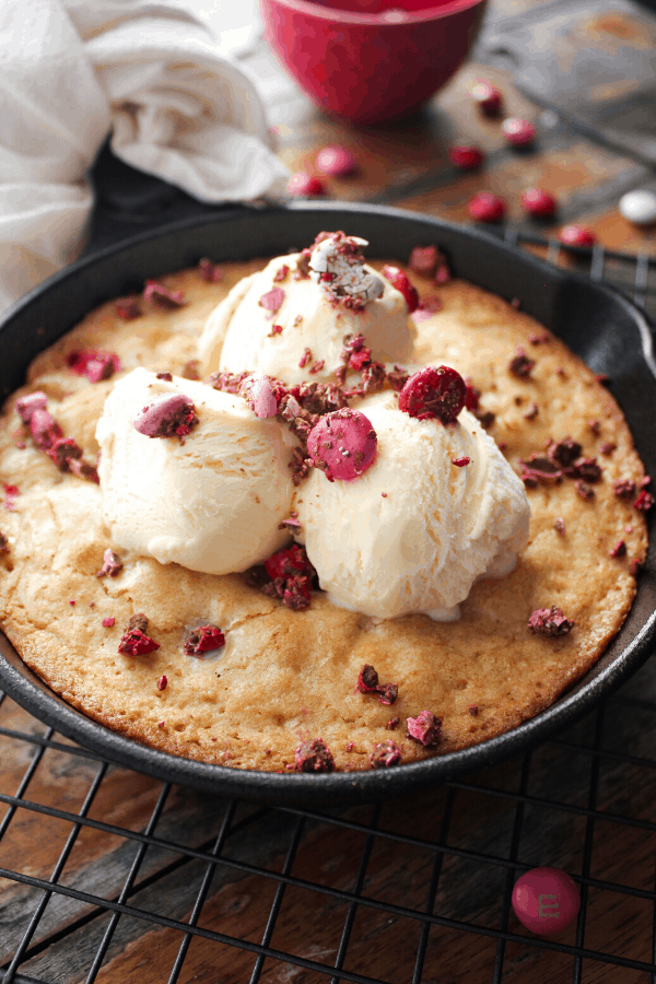 Blondie in a cast-iron skillet topped with three scoops of ice cream and crushed M&M's. 