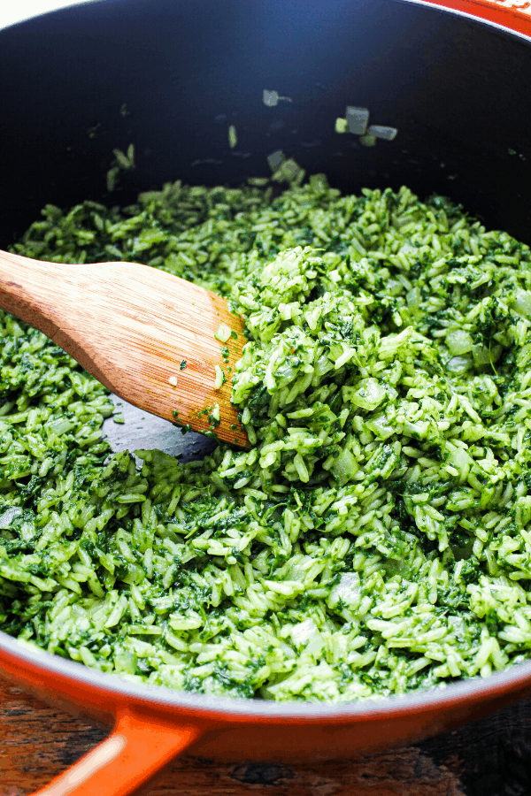close up shot of green rice in orange dutch oven with wooden spoon