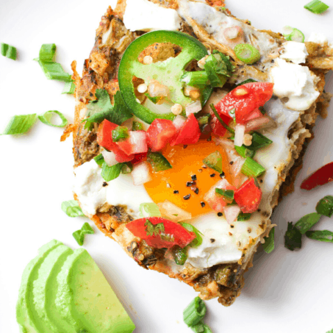 close up shot of slice of huevos rancheros casserole covered in pico on white surface with slices of avocado from above