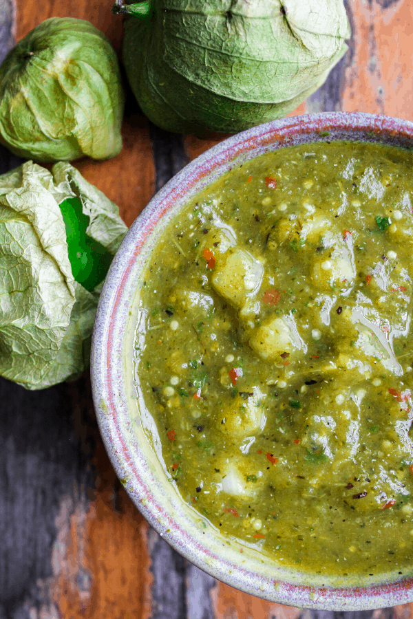 close up of roasted salsa verde in bowl on table with three tomatillos