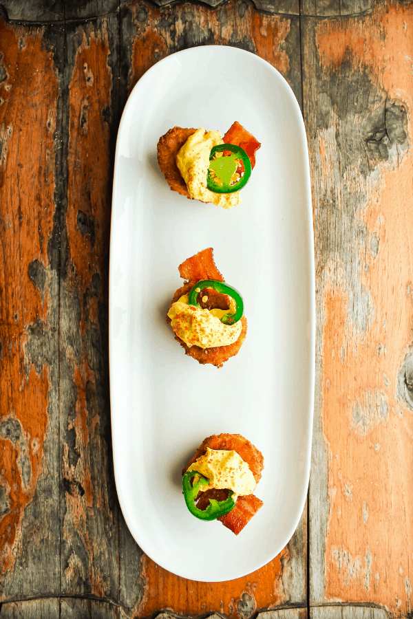 Three deep fried jalapeno popper deviled eggs on a white tray atop a distressed wood surface from above