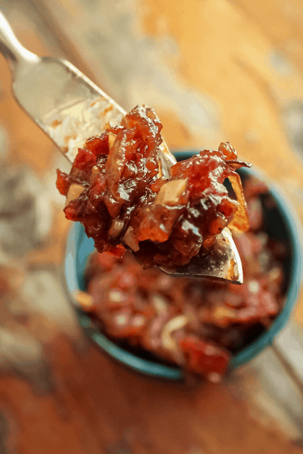 close up of bacon onion jam on serving knife with bowl of jam in background on table