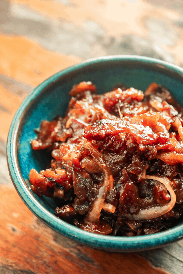 close up of bacon onion jam in small blue bowl on distressed wood surface 
