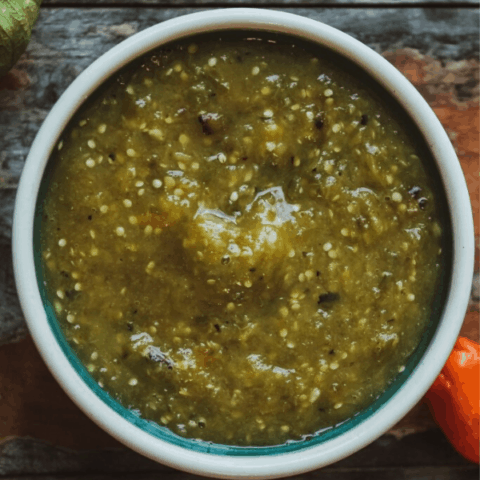 roasted pineapple habanero salsa in a small bowl with tomatillos and habanero on distressed wood surface shot from above