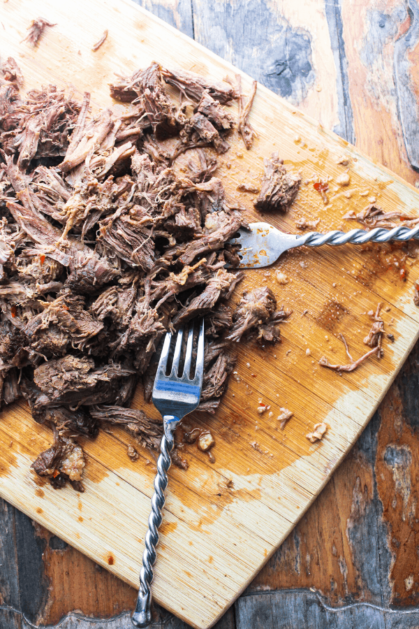 shredded beef on cutting board with two forks 