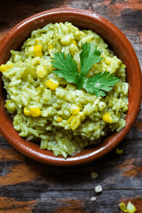 close up of creamy poblano rice w/ corn with sprig of cilantro from above on distressed table 