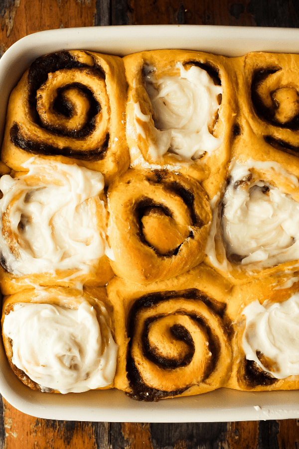 pumpkin cinnamon rolls with chai spice half iced from above in pan