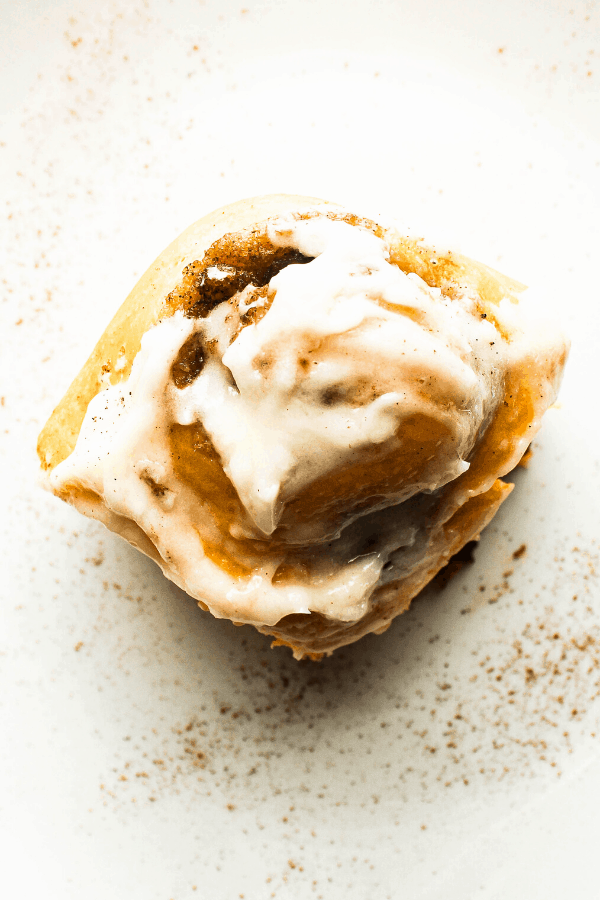 single pumpkin cinnamon rolls with chai spice on white plate sprinkled with cinnamon 