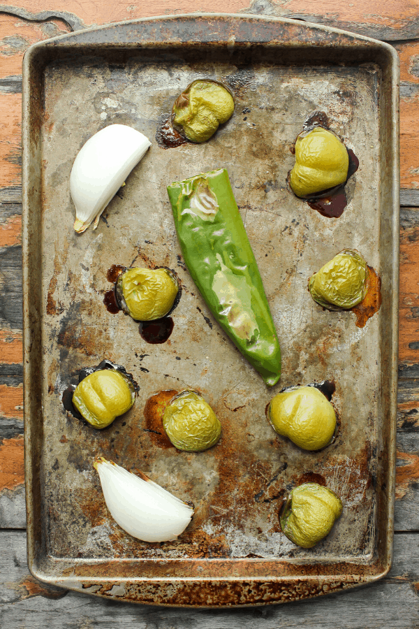 roasted tomatillos, onions, and Anaheim pepper on a baking sheet shot from above. 