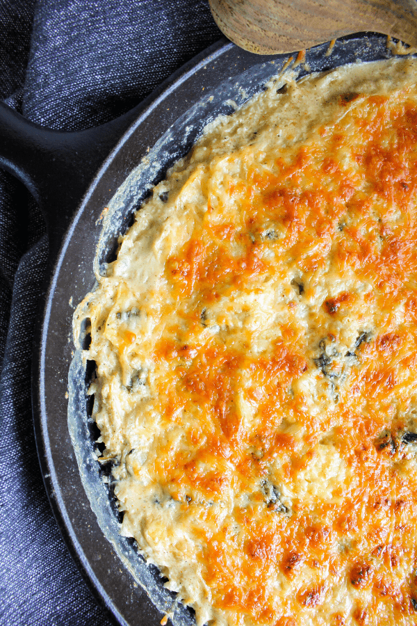 Close-up of half of baked spinach artichoke casserole in cast-iron pan shot from above. 