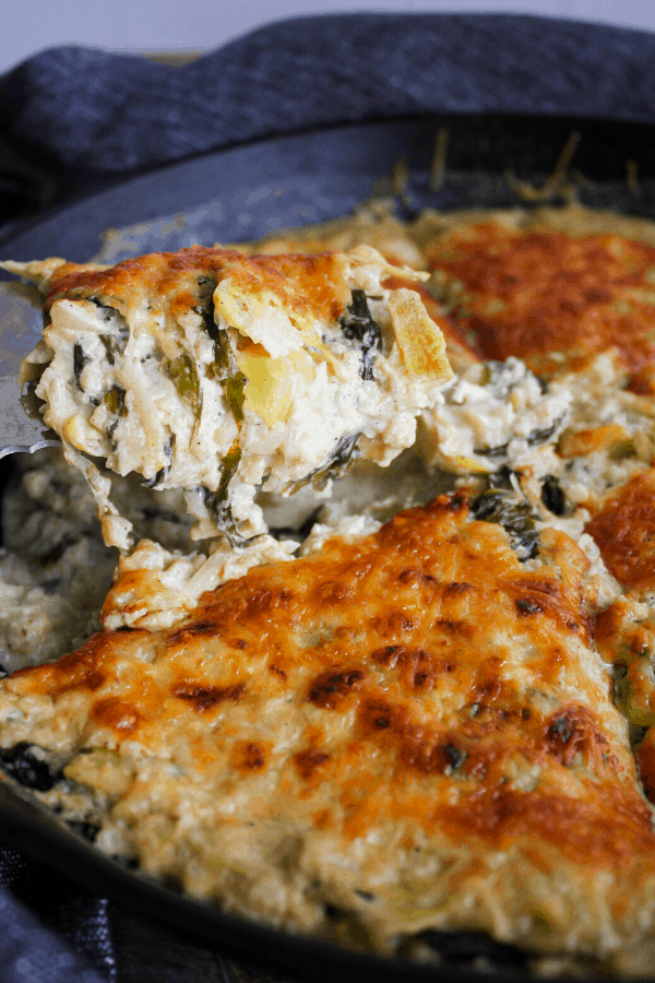 Spatula with slice of casserole above casserole in cast-iron skillet. 