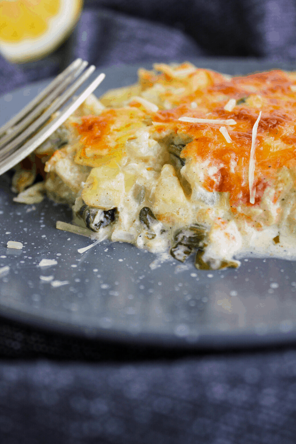 Slice of spinach artichoke casserole on grey plate with fork. 