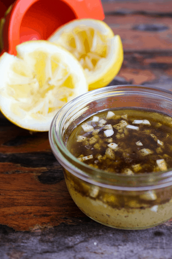 Small jar of lemon dressing with two lemon halves and juicer in background. 
