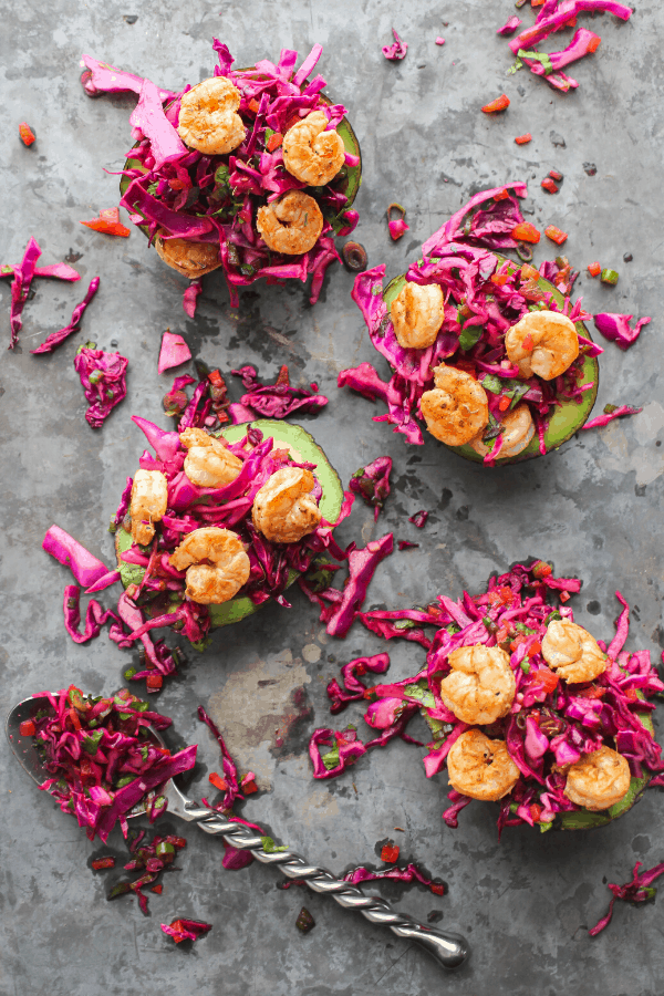 four Mexican slaw & shrimp stuffed avocados on a baking sheet with a spoon of slaw