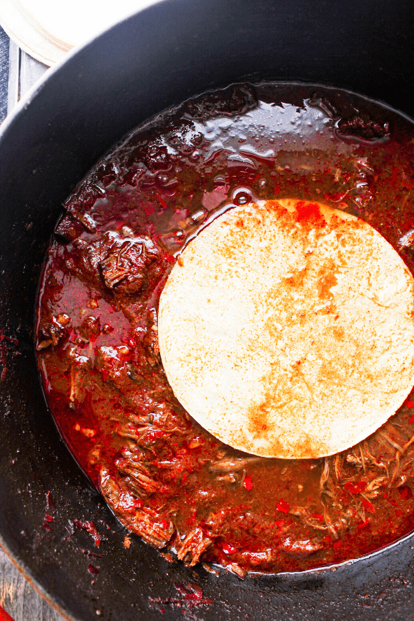 corn tortilla sitting atop beef birria in dutch oven shot from above 