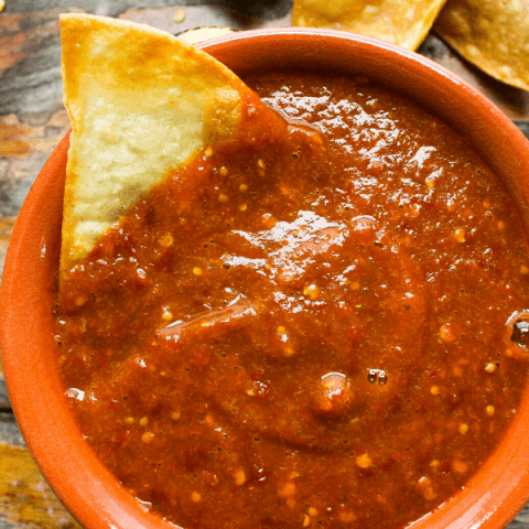 Small bowl of chile de arbol salsa with chip and pile of chips on side.