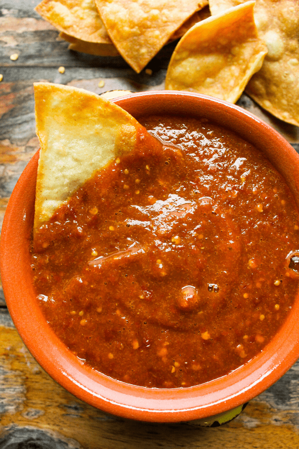 Small bowl of chile de arbol salsa with chip and pile of chips on side. 