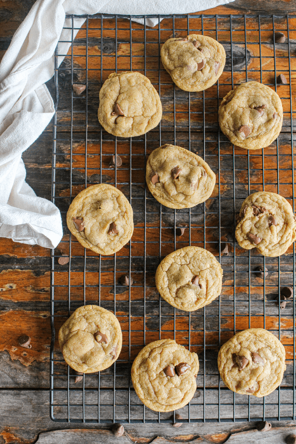 Chocolate chip cookies on wire cooling rack with white towel on distressed wood surface shot from above. 