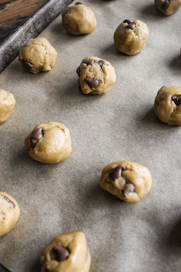 Cookie dough balls on baking sheet covered in parchment paper.