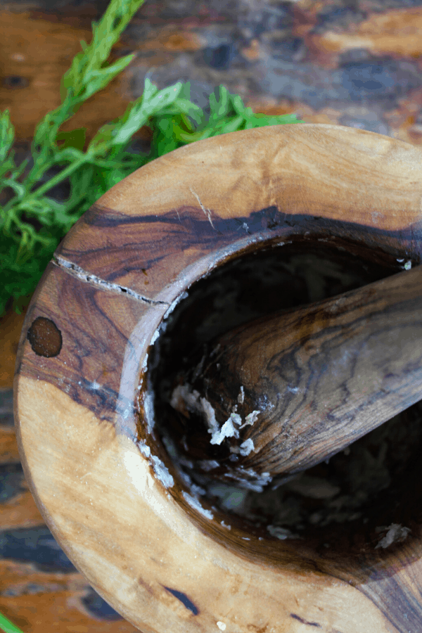 Wooden mortar and pestle with crushed garlic and salt with sprigs of dill in background. 
