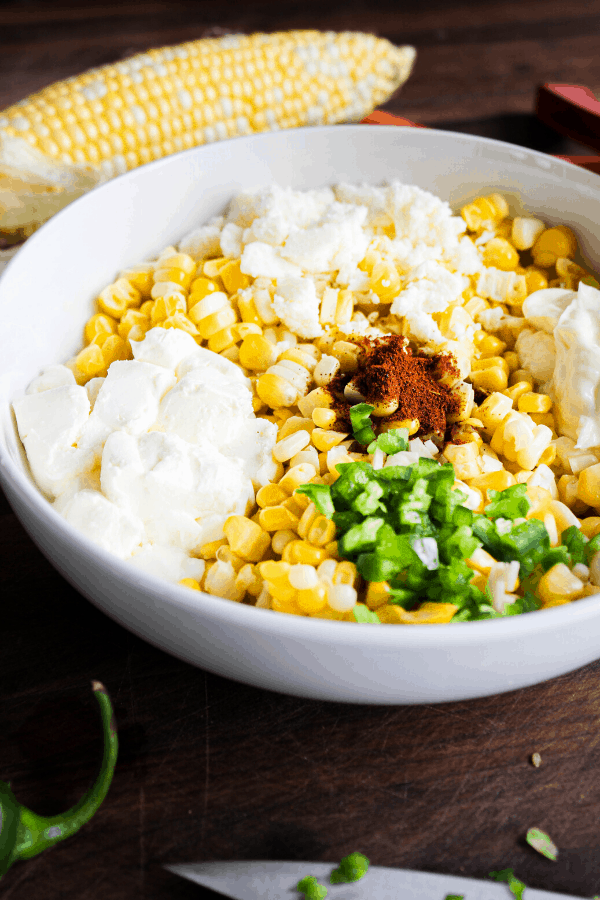 Close up of Mexican street corn ingredients in a bowl with corn cob in background. 