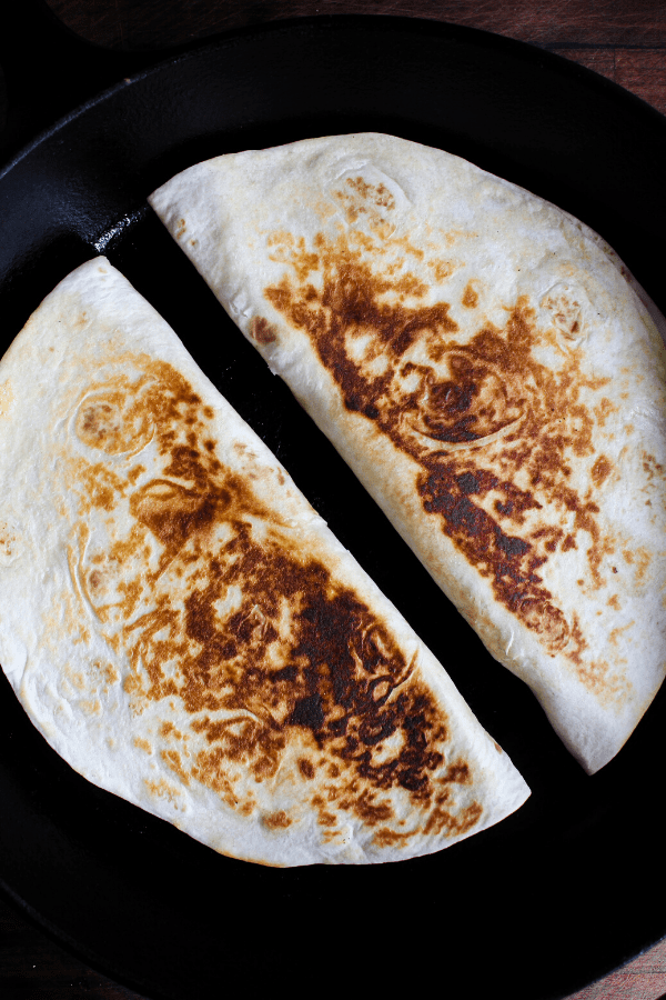 Two grilled quesadillas in a cast-iron skillet shot from above. 