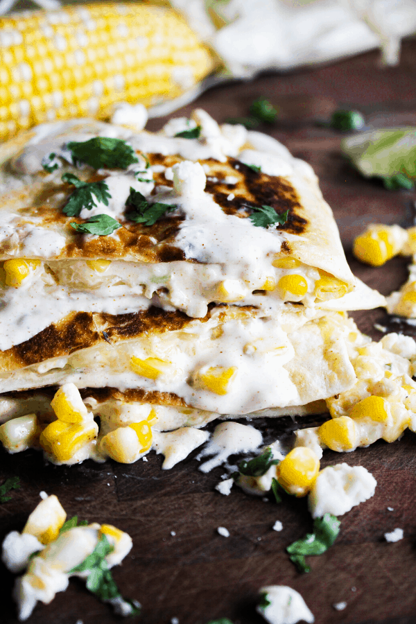 Close up of stacked quesadilla slices drizzled with creamy chipotle sauce with corn cob in background.