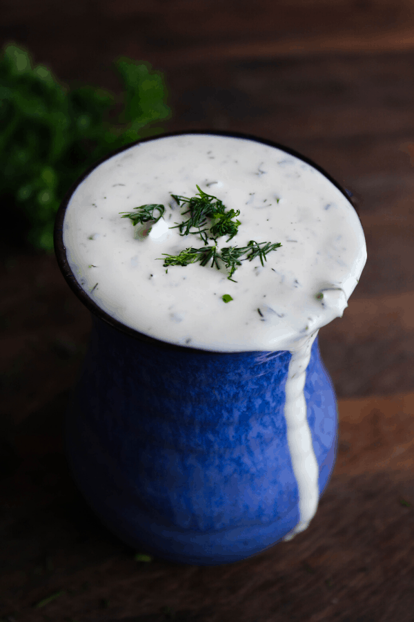 Dill ranch in a blue vase with herbs in background on wood surface.