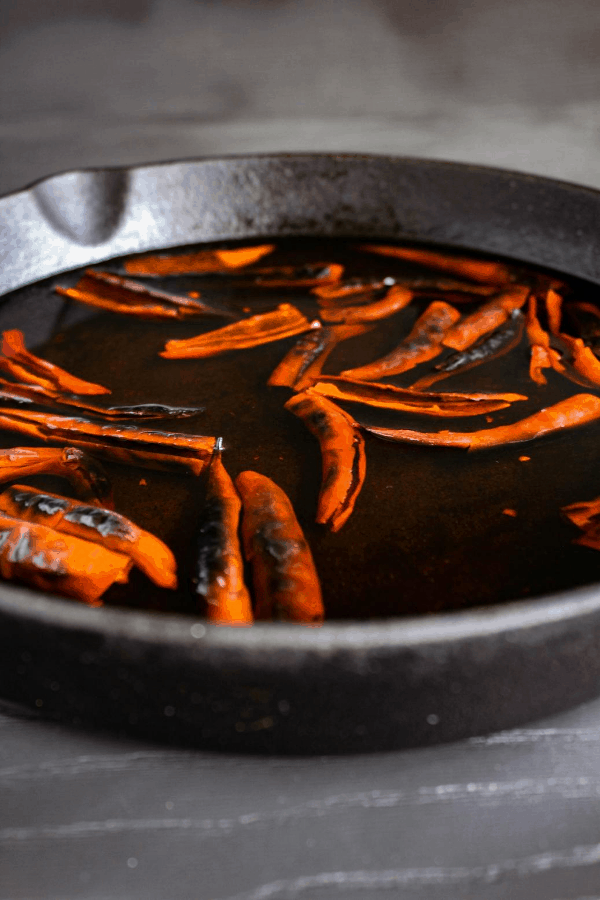 Chile de árbol soaking in water in a cast iron skillet.
