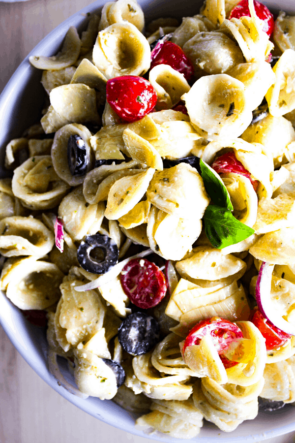 Close up of creamy pesto pasta salad in white bowl shot from above. 