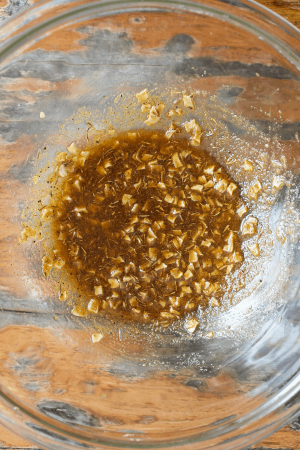 Melted butter, dried onion flakes, and spices mixed together in a clear glass bowl shot from above. 