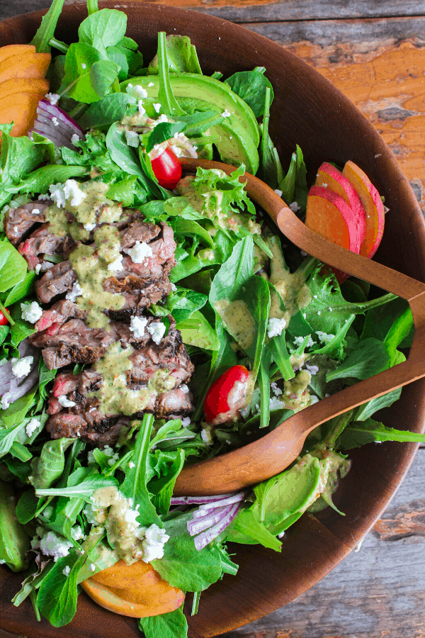 Shot of half of bowl of grilled Steak Salad w/ Habanero Peach Vinaigrette with salad tongs shot from above. 