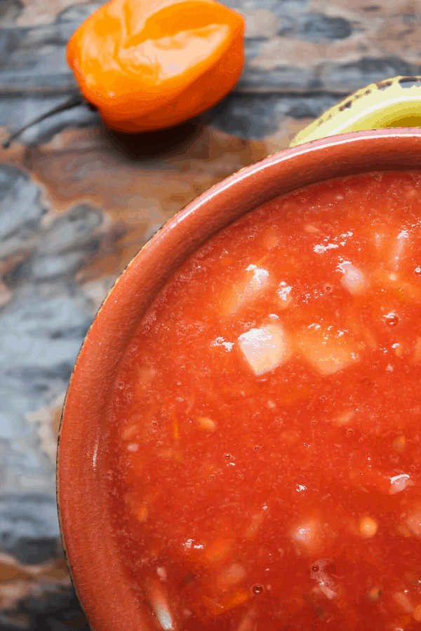 Close-up shot of salsa in a yellow bowl with a habanero pepper on wood surface. 