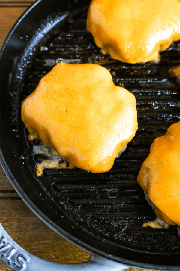 Top down shot of hatch chile burgers with melted cheese in a cast-iron griddle. 