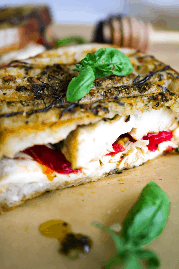 Close-up of chicken caprese panini topped with basil leaves.