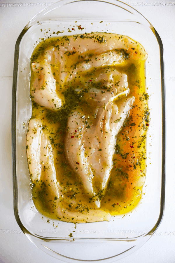 Top down shot of chicken marinating in basil oil. 
