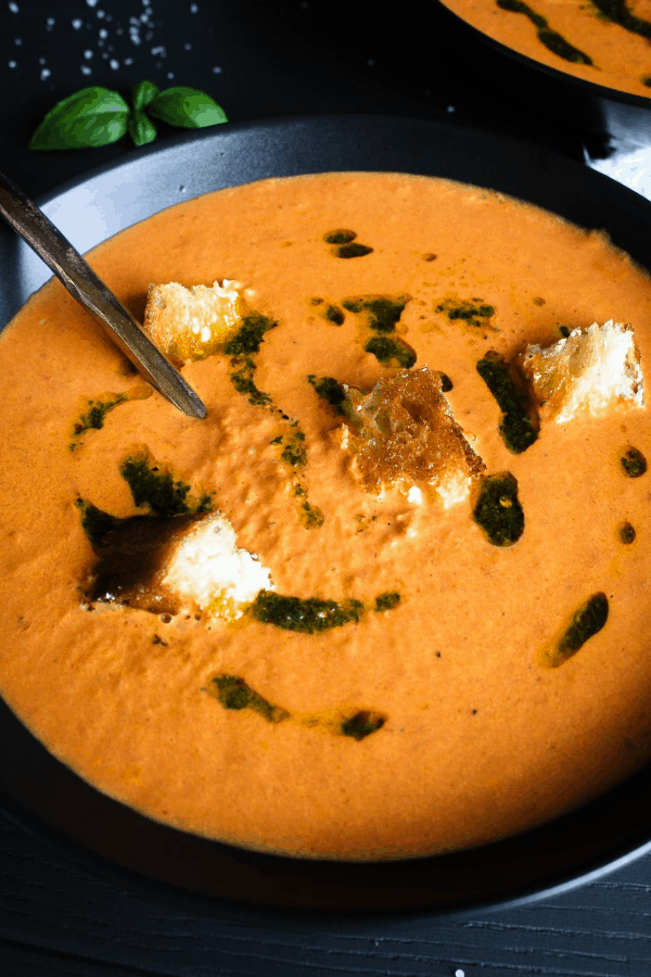 Bowl of tomato soup with spoon with second bowl of soup in background.