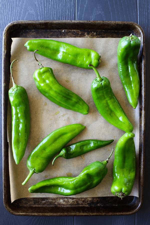 Top down shot of uncooked hatch chiles on a baking sheet lined with parchment paper. 