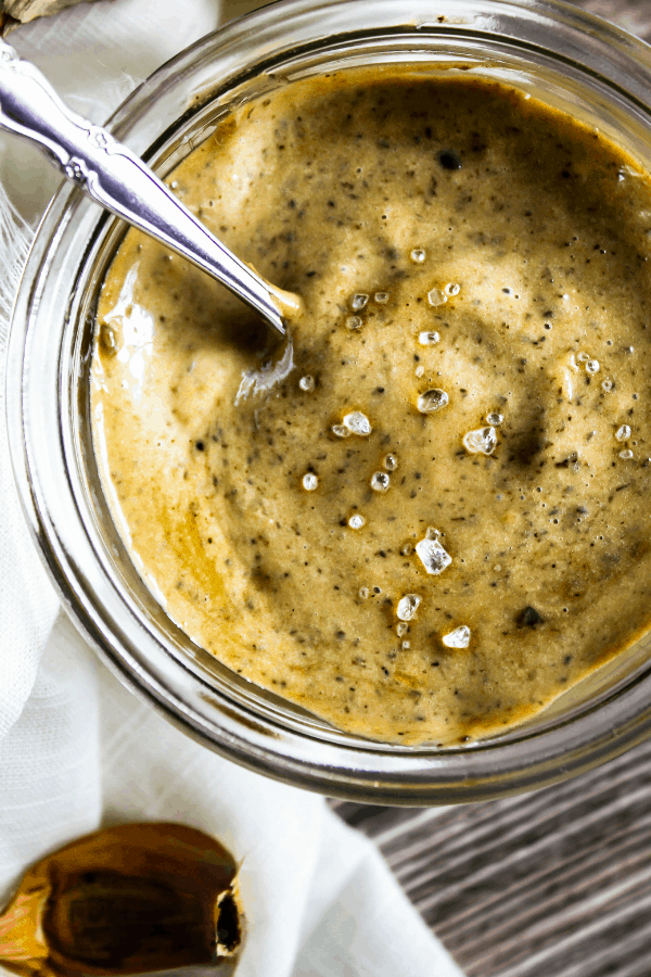 Close-up top down shot of black garlic aioli in a small glass jar with a small silver spoon. 